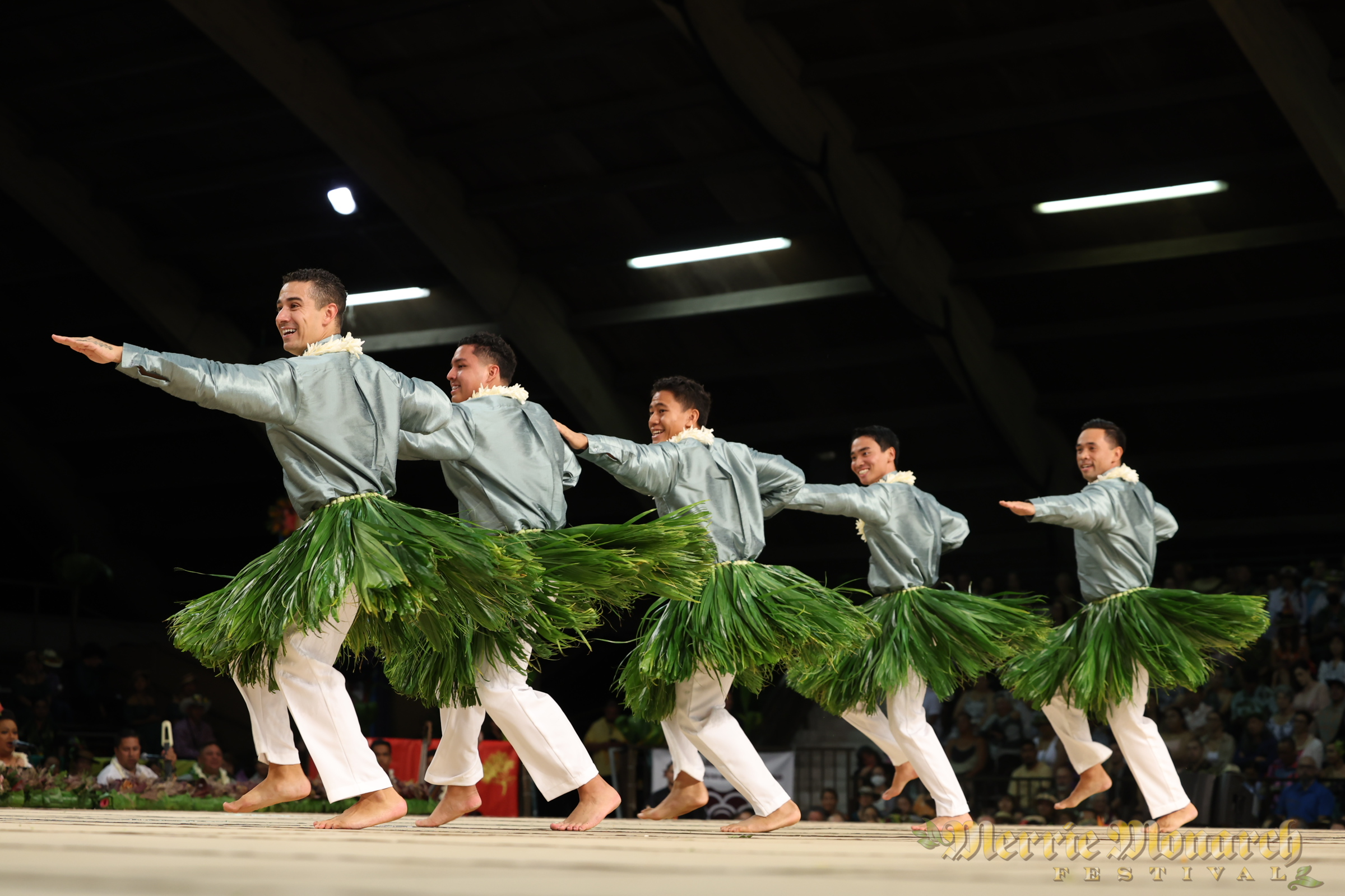 Kane hula dancers, wearing metallic top and ti leaf skirt.