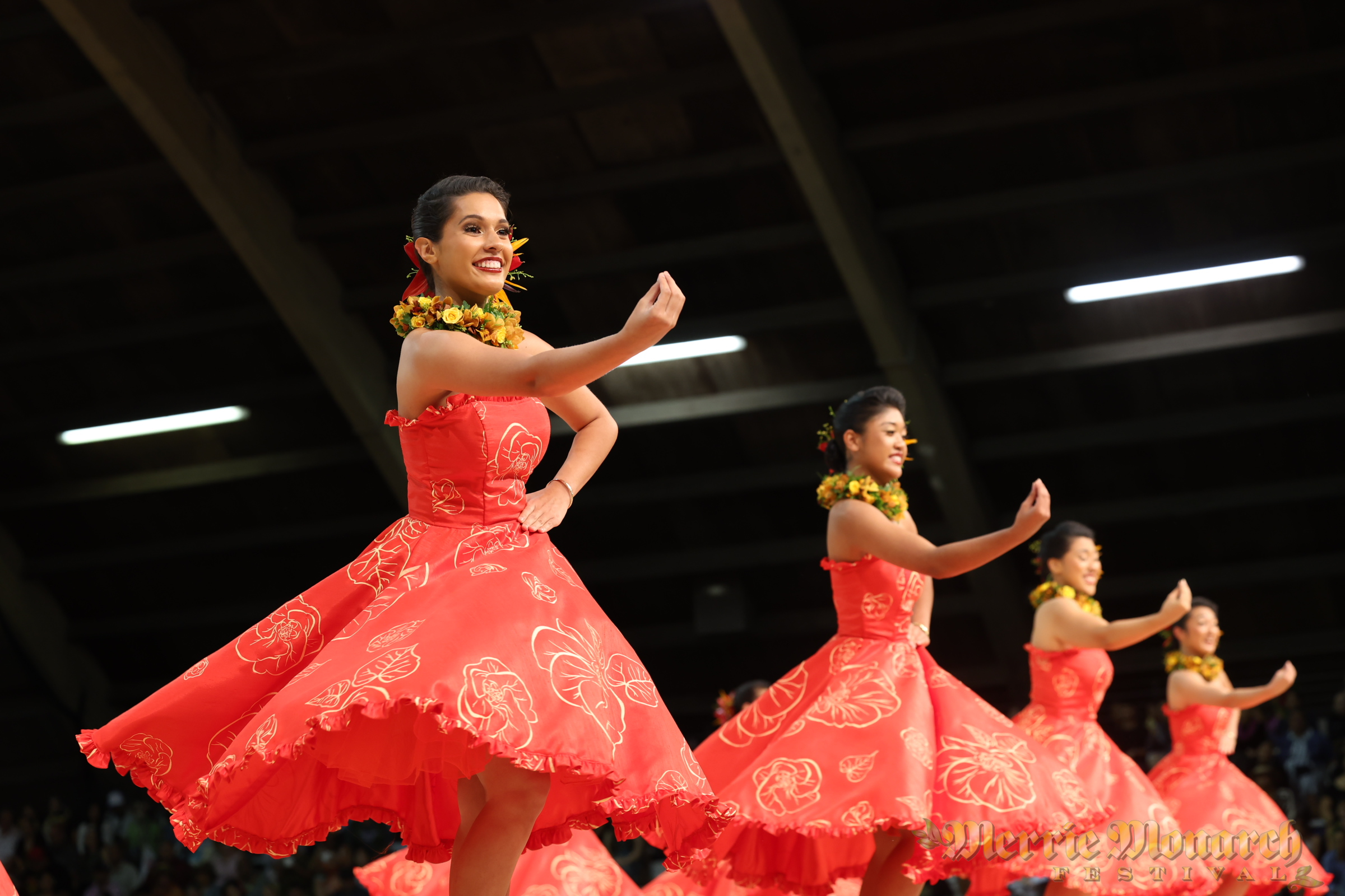 Wahine auana hula dancers adorned in flowers wearing floral print.