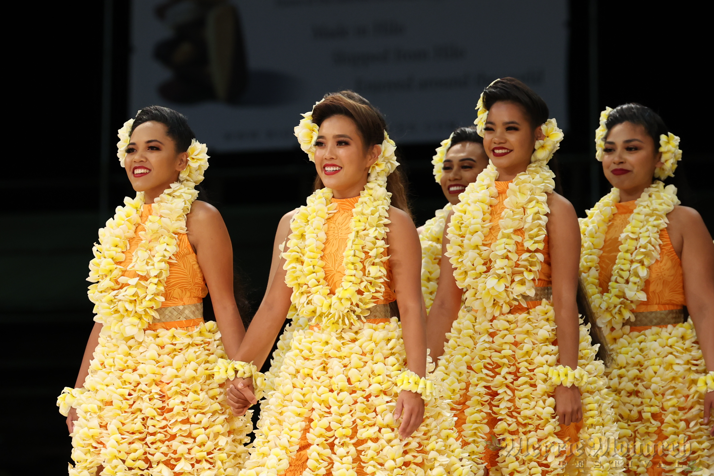 Wahine hula dancers wearing dozens of yellow plumeria flowers.